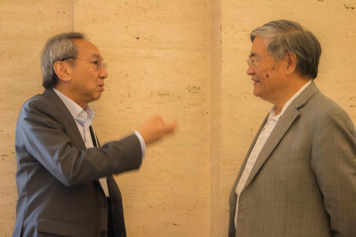 Two men in business attire chat in a hallway.